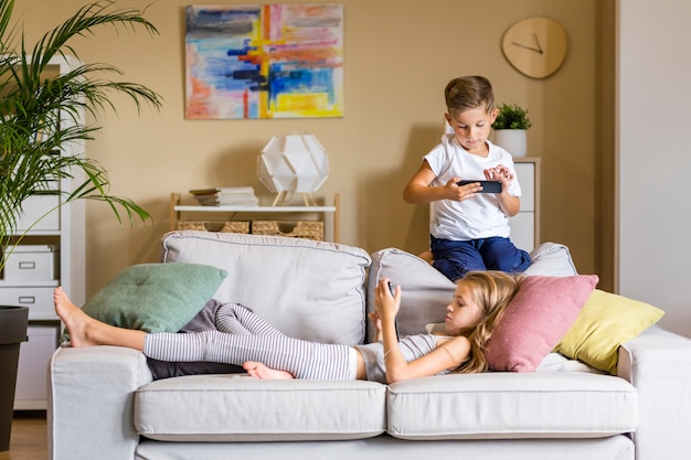 Bruder und Schwester im Wohnzimmer, die ihre Telefone betrachten