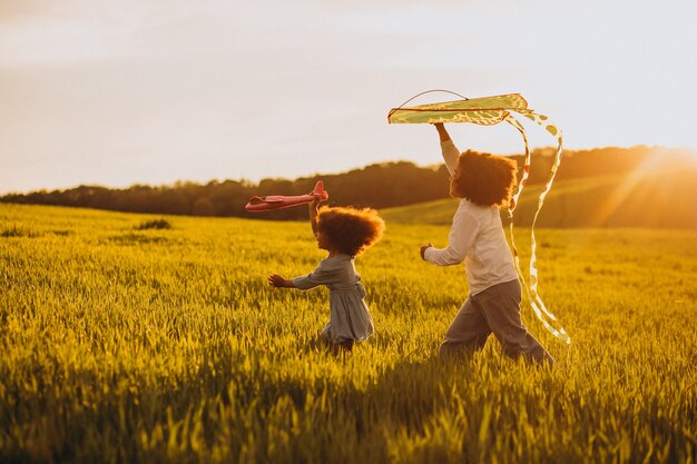 Bruder und Schwester spielen mit Drachen und Flugzeug auf dem Feld bei Sonnenuntergang