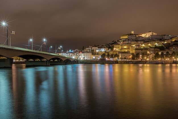 Brücke auf dem Meer in Coimbra mit den Lichtern, die während der Nacht in Portugal auf dem Wasser reflektieren