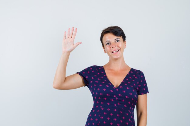 Brünette Frau, die Stoppschild im lila und rot gemusterten Kleid zeigt und optimistisch, Vorderansicht schaut.