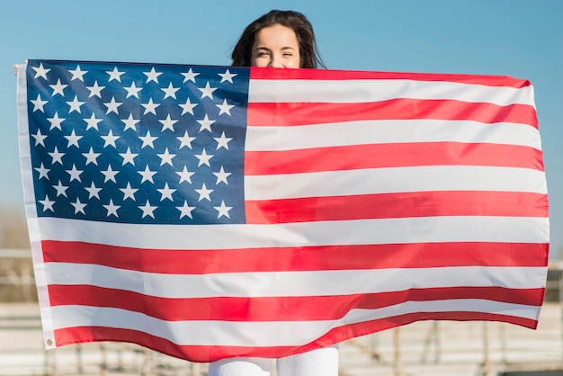 Brünette Frau hält große USA-Flagge über sich