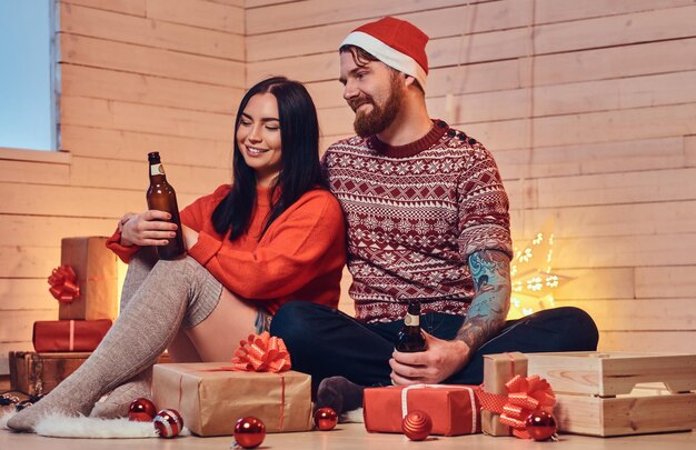 Brünette Frau und bärtiger Hipster-Mann trinken Bier und feiern Weihnachten zu Hause.