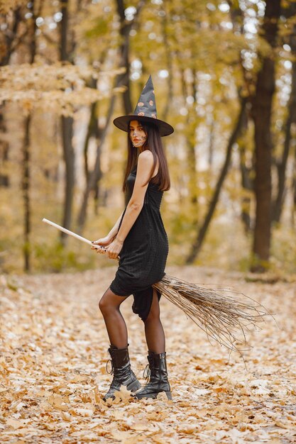 Brünette Hexe des jungen Mädchens im Wald an Halloween. Mädchen, das schwarzes Kleid und Kegelhut trägt. Hexe, die ein Zauberermaterial hält.