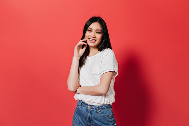 Brünette in T-Shirt und Jeans schaut an der roten Wand nach vorne