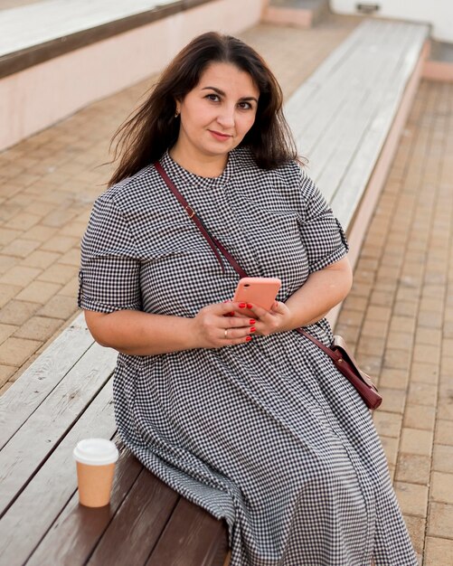 Brünette Smiley-Frau, die ihr Smartphone draußen hält
