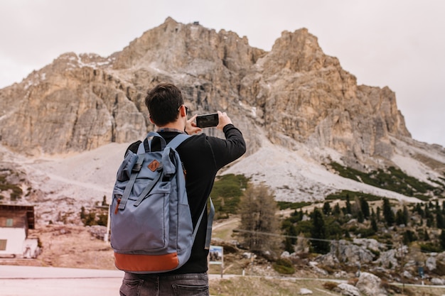 Brünetter junger Mann mit großem Rucksack, der Zeit draußen unter grauem Himmel verbringt, felsige Landschaft genießt