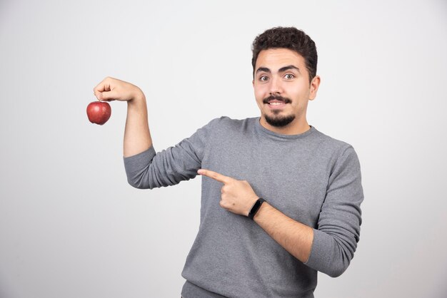 Brünetter Mann, der auf roten Apfel auf grau zeigt.