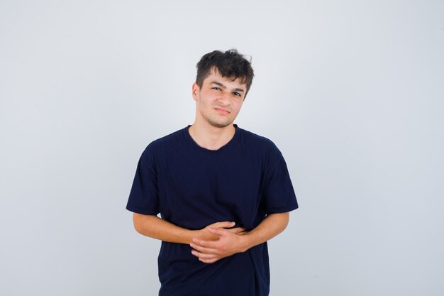 Brünetter Mann, der Hände auf Bauch im dunklen T-Shirt hält und schmerzhafte Vorderansicht schaut.