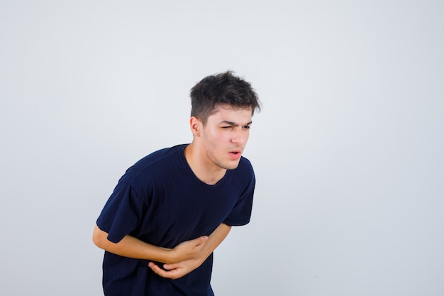 Brünetter Mann, der Hände auf Bauch im dunklen T-Shirt hält und schmerzhafte Vorderansicht schaut.