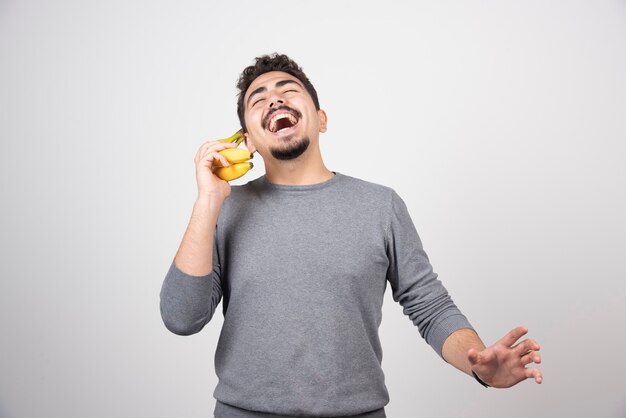 Brünetter Mann, der mit Banane auf Grau spricht.