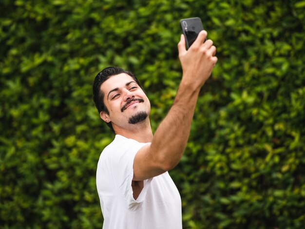 Brünetter Mann, der Selfies gegen ein Grün macht