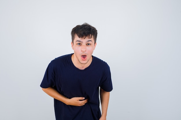 Brünetter Mann im dunklen T-Shirt, das Hand auf Bauch hält und ärgerlich schaut, Vorderansicht.