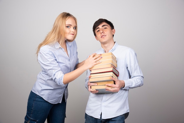 Brünettes Kerlmodell, das einen Stapel Bücher in der Nähe einer blonden Frau trägt