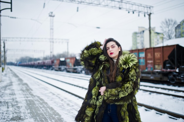 Brünettes Mädchen im grünen Pelzmantel auf der Bahnsteigstation am Wintertag