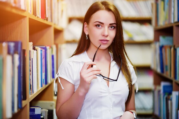 Brünettes Mädchen in der Bibliothek mit Brille auf der Hand, weiße Bluse und schwarzer Minirock Sexy Geschäftsfrau oder Lehrerkonzept