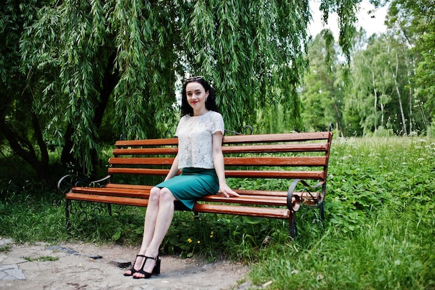 Kostenloses Foto brünettes mädchen in grünem rock und weißer bluse posierte im park auf einer bank sitzend