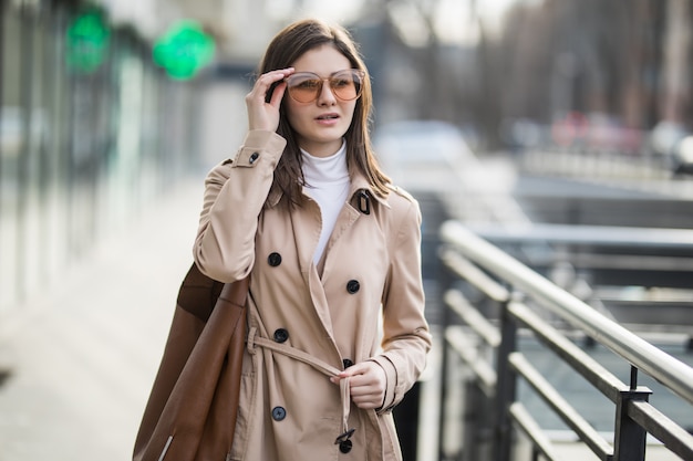 Brünettes Modell mit transparenter Sonnenbrille geht am Herbsttag nach draußen