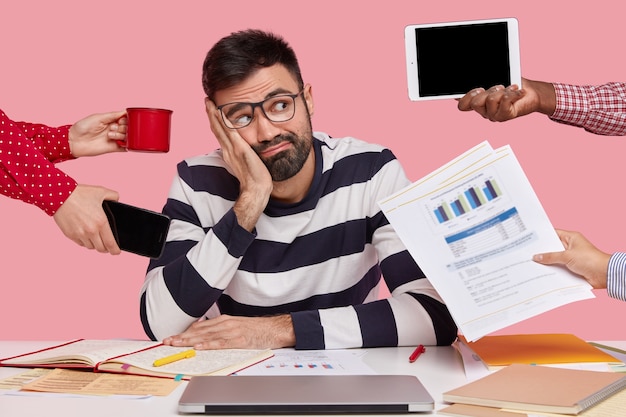 Brunet Mann sitzt am Schreibtisch mit Gadgets und Papieren umgeben