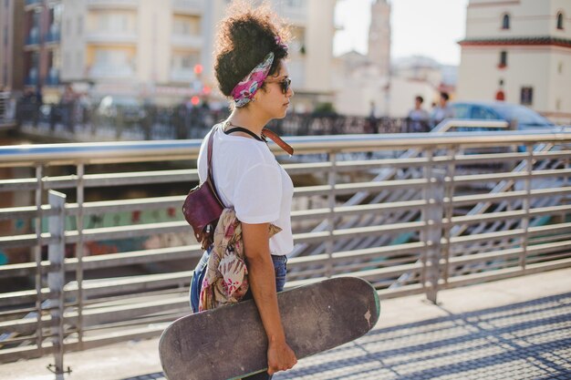 Brunette Mädchen mit Skateboard gehen außerhalb