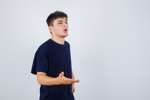 Brunette Mann, der Hand in fragender Geste im T-Shirt streckt und selbstbewusst, Vorderansicht schaut.