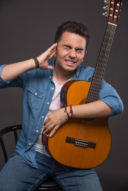 Brunette Mann mit Gitarre mit Kopfschmerzen dunklem Hintergrund.