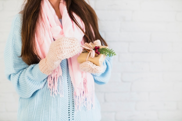 Brunettedame in den Handschuhen und im Schal mit Geschenkbox in den Händen