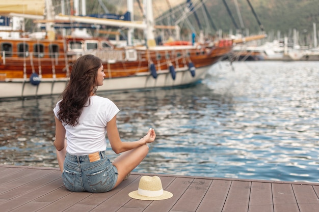 Kostenloses Foto brunettefrau, die auf dem ufer eines hafens sitzt