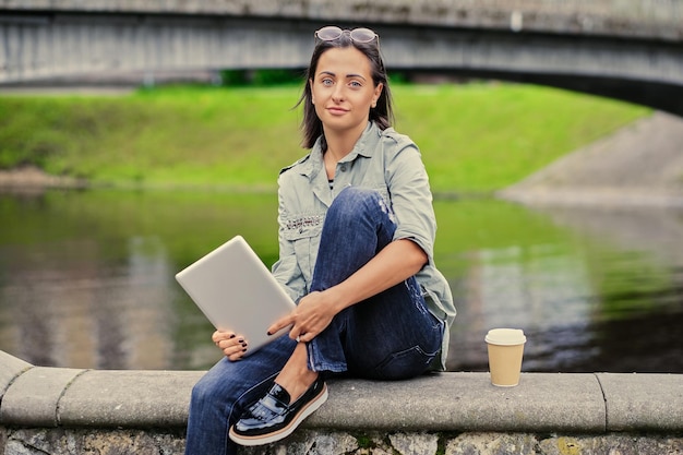 Brunettefrau sitzt auf einer Brücke und hält Tablet-PC.