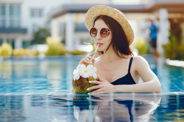 Brunettemädchen, das Kokosnusssaft am Pool trinkt