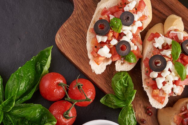 Bruschetta mit Tomaten, Mozzarella und Basilikum auf einem Schneidebrett. Traditionelle italienische Vorspeise oder Snack, Antipasti. Caprese Salat Bruschetta. Draufsicht mit Kopierraum. Flach liegen.