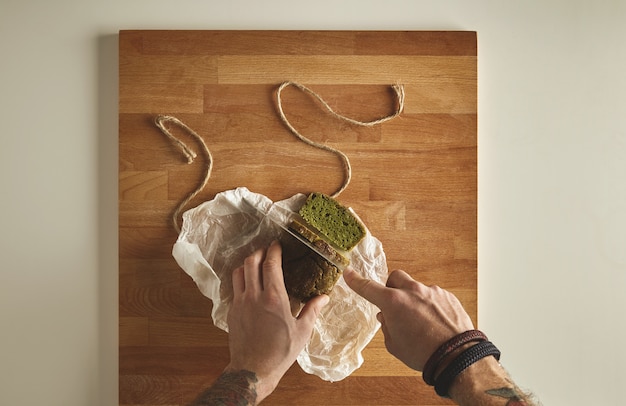 Brutal Mann tätowierte Hände schneiden gesunde Spinat hausgemachte grüne rustikale Brot mit Vintage-Messer auf Scheiben. Weiße Tafeloberansicht des hölzernen Brettes