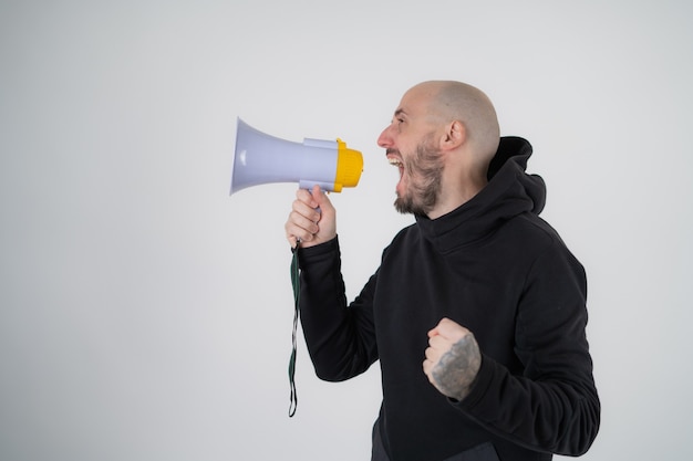 Brutaler Mann im schwarzen Hoodie isoliert mit einem Lautsprecher-Megaphon, das schreit