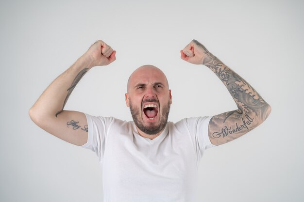 Brutaler Mann in weißen T-Shirt-Tattoos springt Spaß, Gewinnergeste