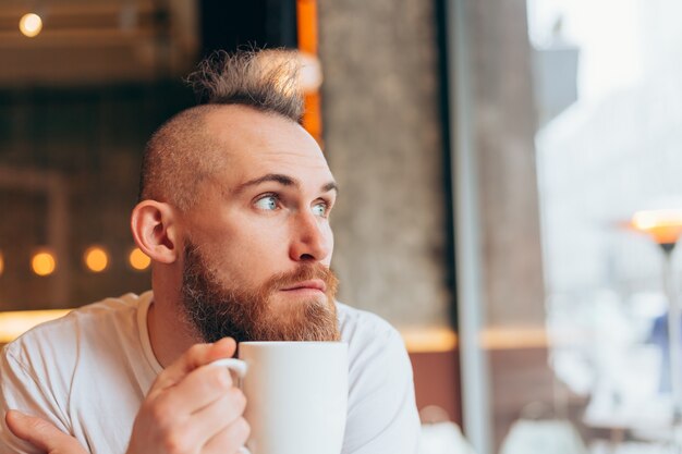 Brutaler Mann von europäischem Aussehen in einem Café am Morgen mit einer Tasse heißen Kaffees