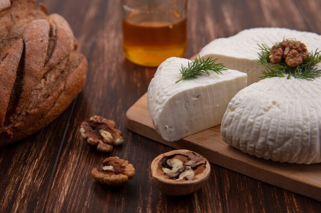 Bryndza-Käse von der Seitenansicht auf einem Ständer mit Walnüssen und einem Laib Brot auf einem hölzernen Hintergrund