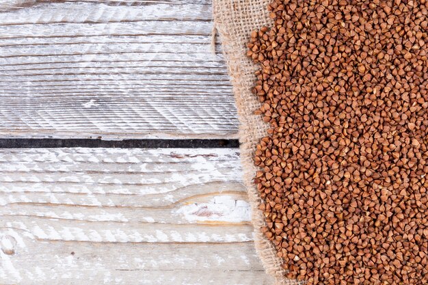 Buchweizen auf einem Sack und weißem Holz. Draufsicht. Platz für Text