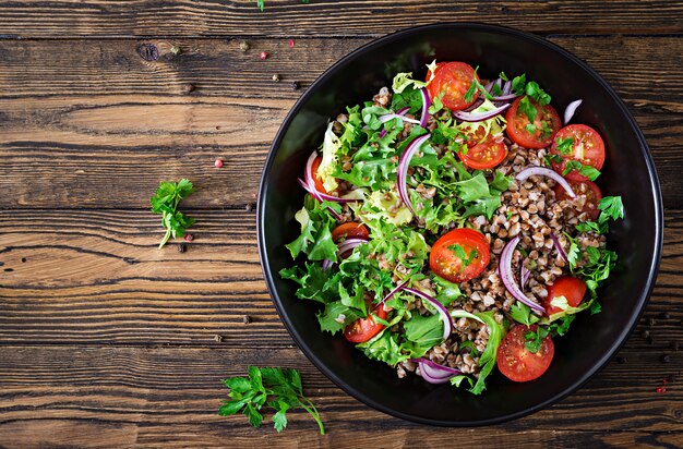 Buchweizensalat mit Kirschtomaten, roten Zwiebeln und frischen Kräutern. Veganes Essen. Diät-Menü. Ansicht von oben. Flach liegen