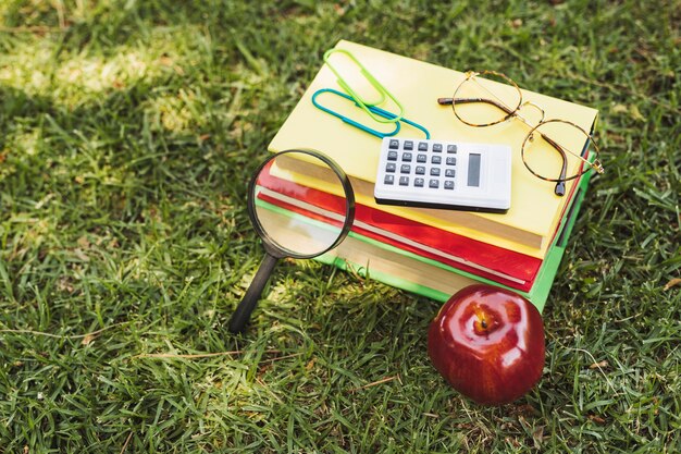 Bücher mit optischen Geräten, Taschenrechner und Apfel auf Gras