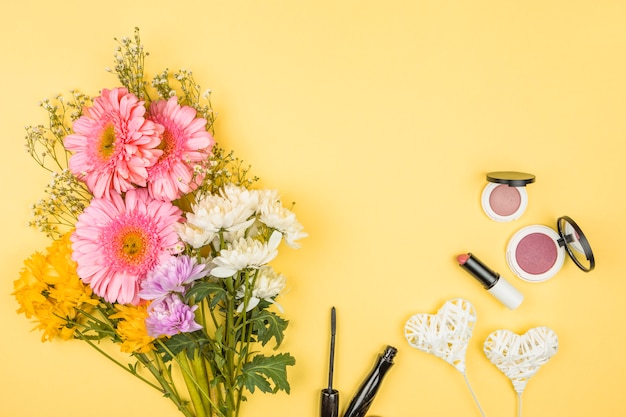 Bündel frische Blumen nahe dekorativen Herzen auf Zauberstäben und Lippenstiften mit Pulvern