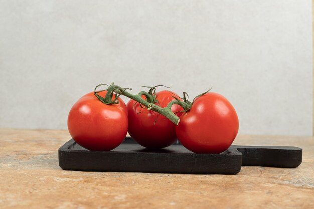 Bündel frische, rote Tomaten mit grünen Stielen auf dunklem Teller