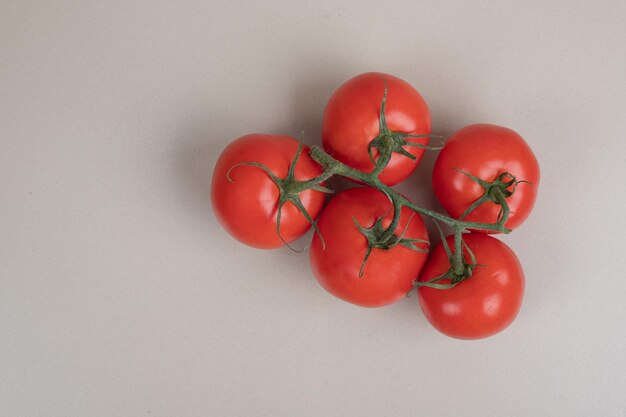 Bündel frische, rote Tomaten mit grünen Stielen auf weißem Tisch.