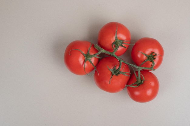 Bündel frische, rote Tomaten mit grünen Stielen auf weißem Tisch.