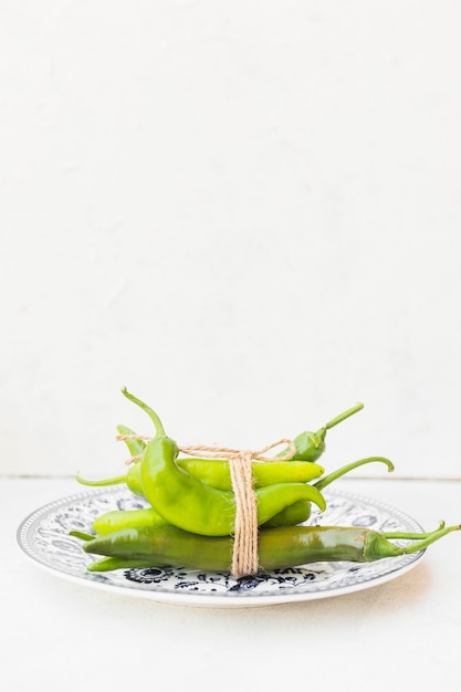 Bündel grüner Paprika gebunden mit Schnur auf keramischer Platte gegen weißen Hintergrund
