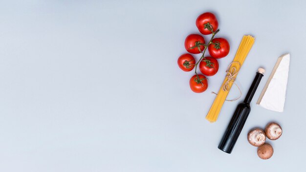 Bündel rohe Spaghettiteigwaren; Tomate; Pilz; Käse- und Ölflasche zum Zubereiten von leckeren Nudeln