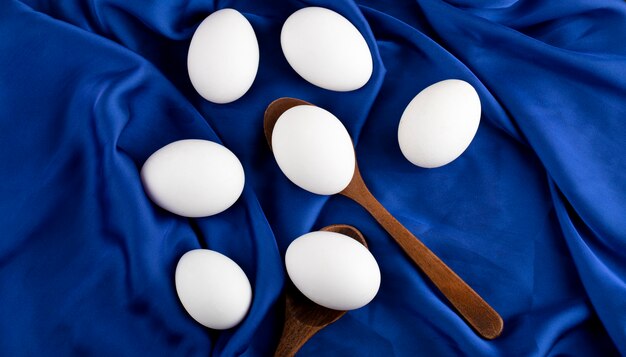 Bündel roher Eier mit Holzlöffel auf blauem Satinstoff.