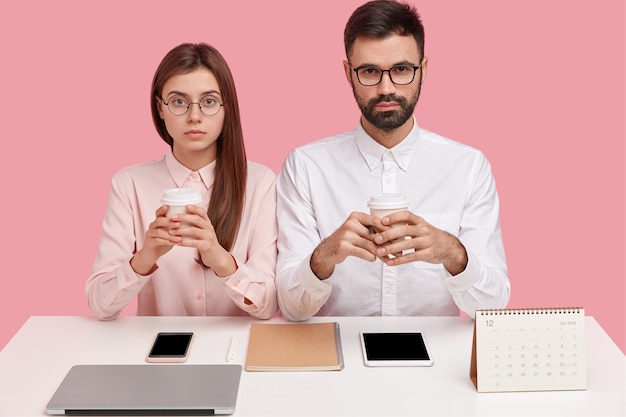 Büro-Perfektionisten sitzen am Desktop und halten Handys, haben ernsthafte Gesichtsausdrücke, tragen ein elegantes Hemd und haben die richtige Reihenfolge auf dem Schreibtisch
