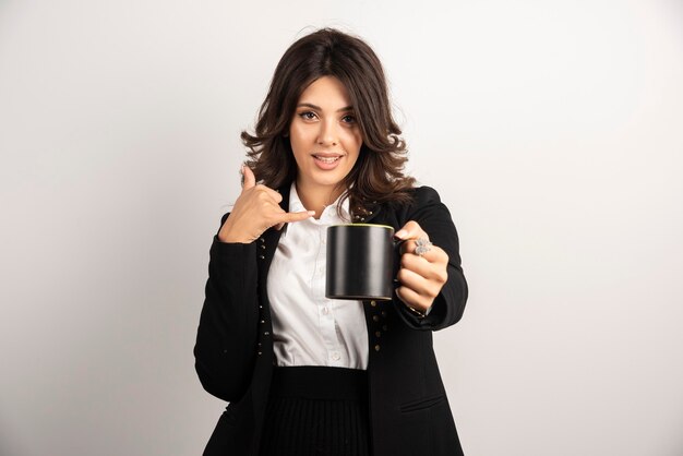 Büroangestellte bietet eine Tasse Tee an und gestikuliert, sie anzurufen