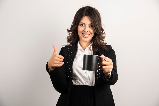 Büroangestellte bietet eine Tasse Tee an und gibt Daumen hoch