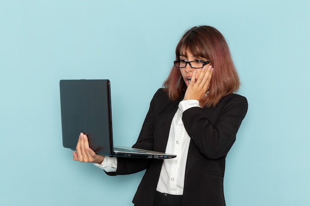 Büroangestellte der Vorderansicht im strengen Anzug unter Verwendung ihres Laptops auf hellblauer Oberfläche