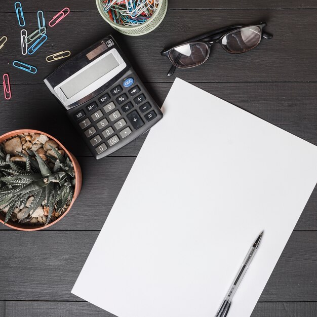 Büroklammern; Taschenrechner; Brille; Topfpflanze mit Stift auf leeres weißes Papier